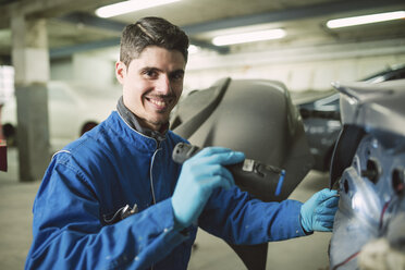 Porträt eines lächelnden Mechanikers, der ein Auto mit einer Taschenlampe in einer Werkstatt inspiziert - RAEF01994