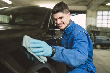 Smiling man cleaning a car in a workshop - RAEF01996