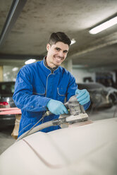 Portrait of smiling man polishing the hood of a car in a workshop - RAEF02000