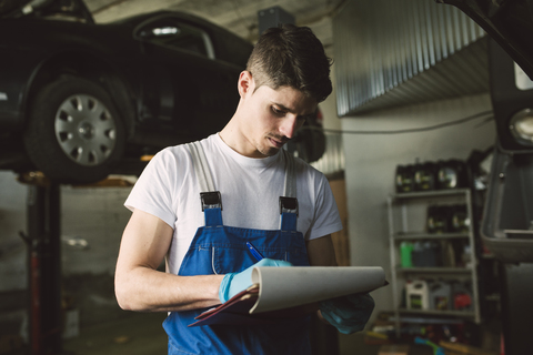 Mechaniker mit Klemmbrett und Checkliste in seiner Werkstatt, lizenzfreies Stockfoto