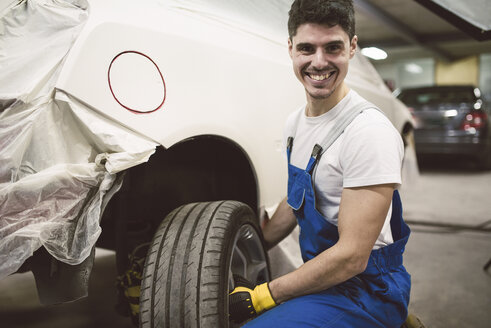 Porträt eines lächelnden Mechanikers, der einen Autoreifen in seiner Werkstatt wechselt - RAEF02023