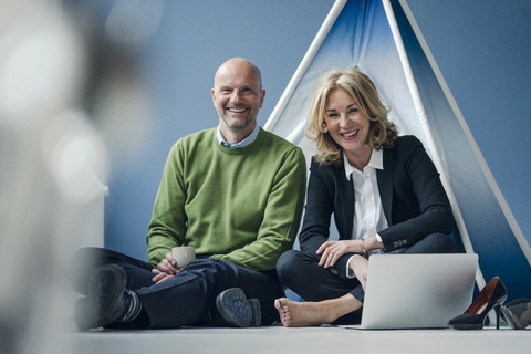 Glücklicher Geschäftsmann und Geschäftsfrau, die mit einem Laptop in einem Tipi sitzen, lizenzfreies Stockfoto