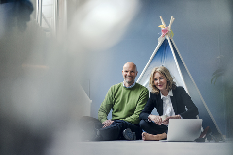 Ein lächelnder Geschäftsmann und eine Geschäftsfrau sitzen mit einem Laptop in einem Tipi, lizenzfreies Stockfoto