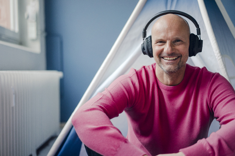 Porträt eines lächelnden reifen Mannes mit Kopfhörern, der in einem Tipi sitzt, lizenzfreies Stockfoto