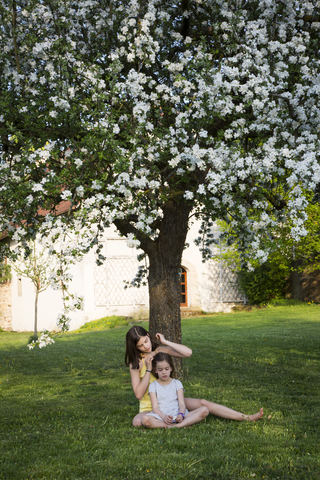 Two girls sitting in front of blossoming apple tree in the garden stock photo