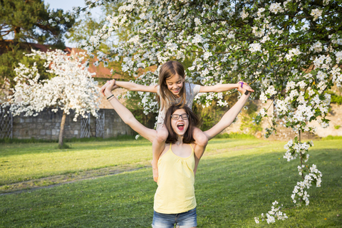 Mädchen trägt kleine Schwester auf den Schultern im Garten, lizenzfreies Stockfoto