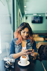 Lächelnde Frau sitzt in einem Café und schaut auf ihr Handy - JPF00312