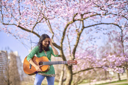 Glückliche junge Frau mit Gitarre in einem Park an einem Kirschblütenbaum - BEF00021