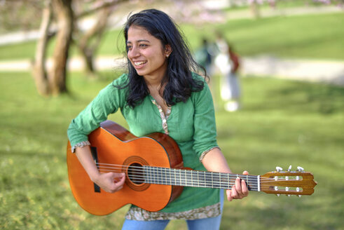 Glückliche junge Frau spielt Gitarre im Park - BEF00022