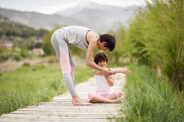 Mutter erklärt ihrer Tochter auf der Strandpromenade die Yoga-Position - JSMF00182