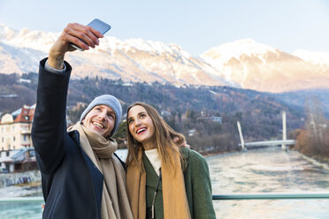 Austria, Innsbruck, portrait of happy young couple taking selfie with smartphone in winter - WPEF00225