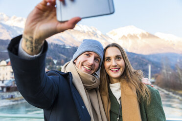 Austria, Innsbruck, portrait of happy young couple taking selfie with smartphone in winter - WPEF00226