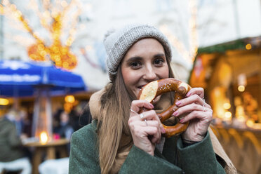 Portrait of smiling young woman with pretzel at Christmas market - WPEF00236