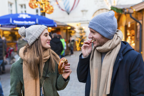 Young couple eating pretzel together at Christmas market - WPEF00237