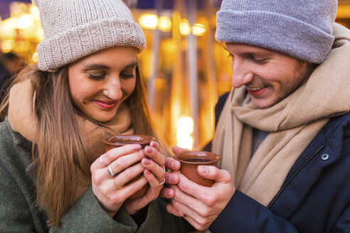 Glückliches junges Paar mit Tassen Glühwein auf dem Weihnachtsmarkt - WPEF00241