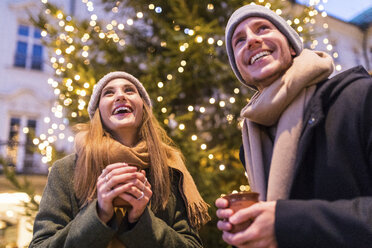 Lachendes junges Paar beim Glühweintrinken auf dem Weihnachtsmarkt - WPEF00246