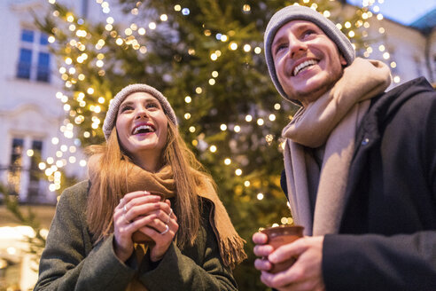 Lachendes junges Paar beim Glühweintrinken auf dem Weihnachtsmarkt - WPEF00246
