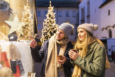 Young couple with cups of mulled wine looking at shop window at Christmas time - WPEF00247