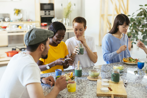 Freunde sitzen am Küchentisch, essen und trinken, lizenzfreies Stockfoto