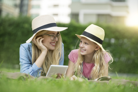 Happy mother and daughter with book and smartphone in urban city garden stock photo