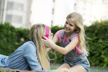 Happy mother and daughter listening to music together in garden - SBOF01478