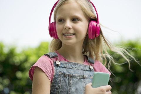 Nettes blondes Mädchen hört Musik mit rosa Kopfhörern im Garten, lizenzfreies Stockfoto