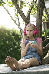 Nettes blondes Mädchen hört Musik mit rosa Kopfhörern im Garten - SBOF01480