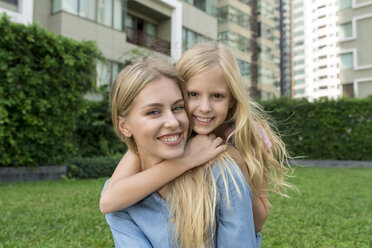 Happy mother and daughter hugging and smiling in urban city garden - SBOF01483