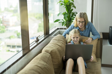 Mother and daughter in modern living room on a couch with laptop and credit card - SBOF01491