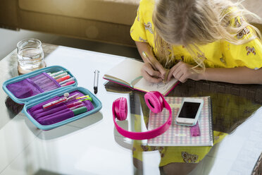 Girl doing her homework writing in booklet on table in living room - SBOF01499