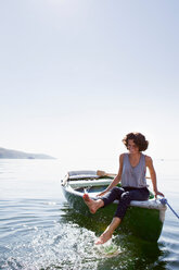 Frau baumelt mit den Füßen vom Boot im See - CUF00881