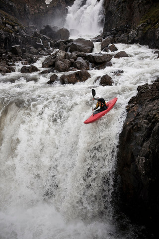 Man canoeing over rocky waterfall stock photo