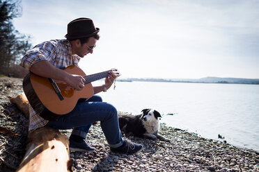Mann spielt Gitarre mit Hund am Bach - CUF00895