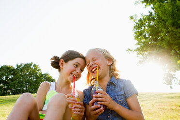 Lachende Mädchen, die im Freien Saft trinken - CUF00906