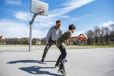 Vater und Sohn spielen Basketball auf einem Platz im Freien - DIGF04161