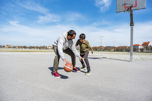 Vater und Sohn spielen Basketball auf einem Platz im Freien - DIGF04163