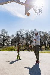 Vater und Sohn spielen Basketball auf einem Platz im Freien - DIGF04164