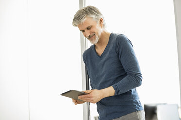 Älterer Mann, der in seinem Büro steht und ein digitales Tablet benutzt - FMKF05059