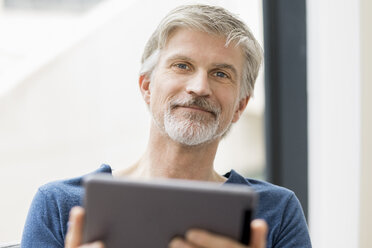 Mature man sitting in his office, using digital tablet - FMKF05071