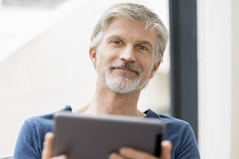 Älterer Mann, der in seinem Büro sitzt und ein digitales Tablet benutzt - FMKF05071