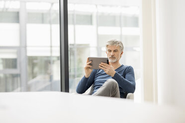 Älterer Mann, der in seinem Büro sitzt und ein digitales Tablet benutzt - FMKF05072