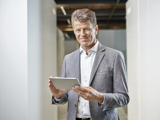 Portrait of smiling businessman with tablet on office floor - CVF00344