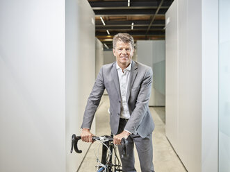 Portrait of smiling businessman with bicycle on office floor - CVF00346