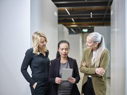 Three businesswomen sharing tablet on office floor - CVF00353