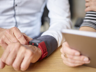 Close-up of businessman and businesswoman with smartwatch and tablet in office - CVF00362