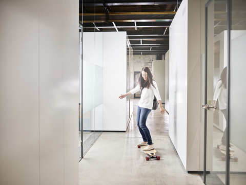 Frau fährt Longboard auf dem Büroboden, lizenzfreies Stockfoto
