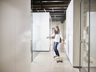 Woman riding longboard on office floor - CVF00394