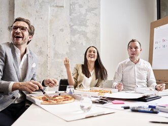 Lachende Kollegen in der Mittagspause mit Pizza im Konferenzraum - CVF00396