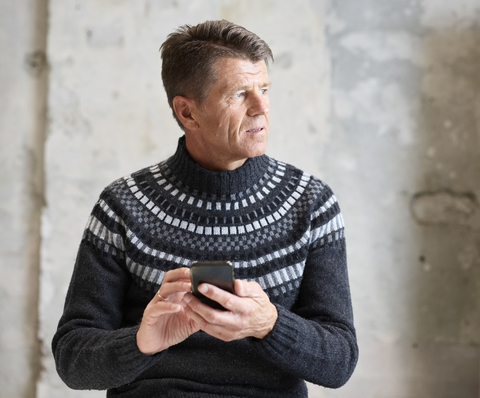 Mann trägt Pullover und hält Mobiltelefon, lizenzfreies Stockfoto