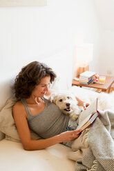 Woman reading with dog in bed - CUF01099